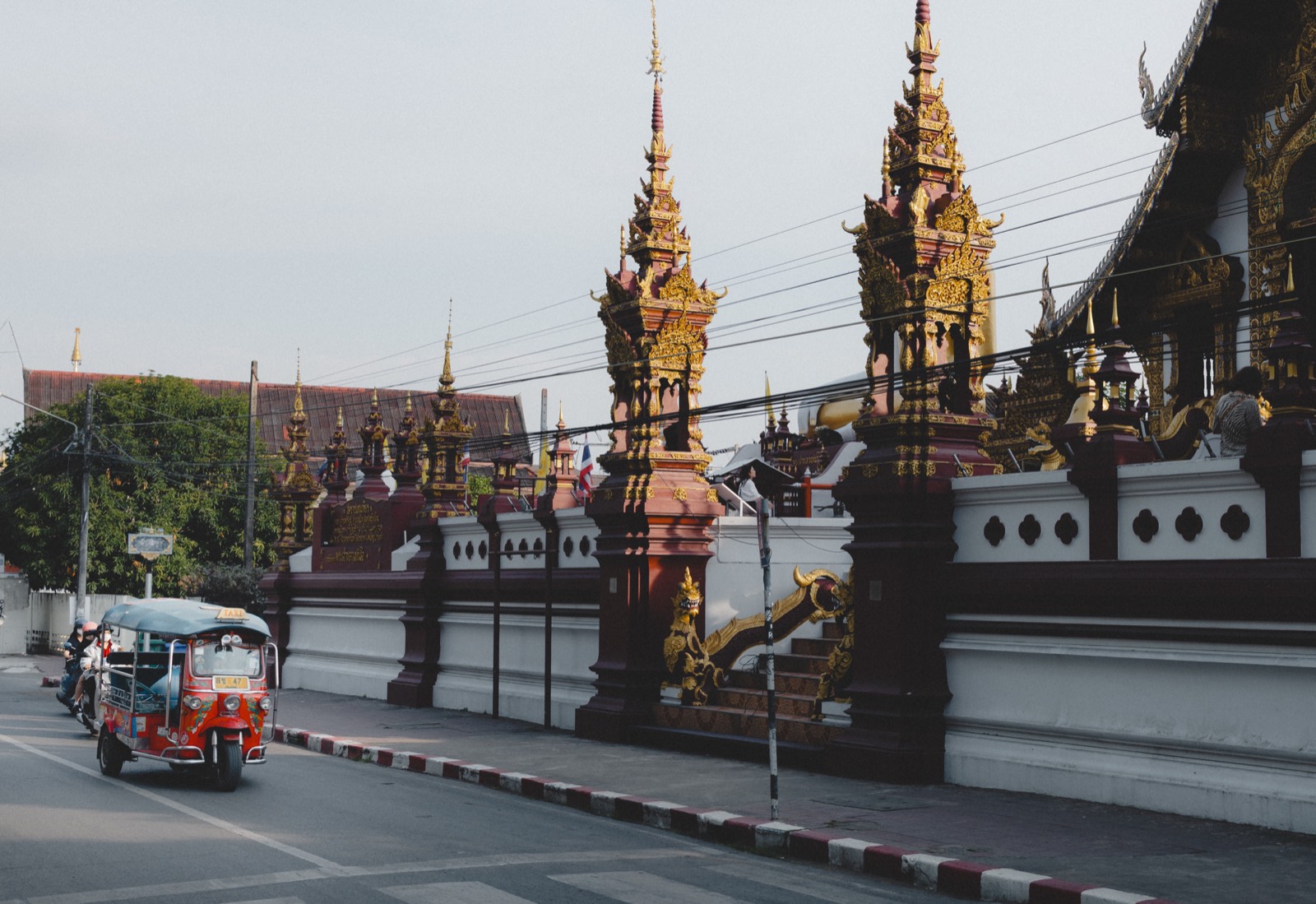Golden temple spires and a tuk-tuk on a street in Thailand